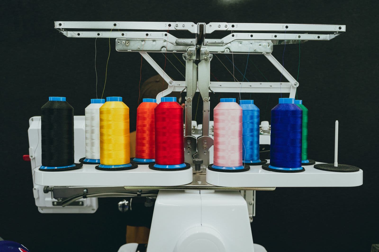 A row of coloured thread cones loaded on an embroidery machine head.